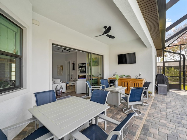 view of patio with glass enclosure, outdoor dining area, and a ceiling fan