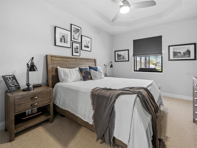 bedroom with light carpet, ceiling fan, a tray ceiling, and baseboards