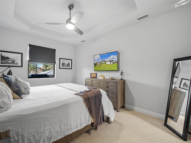 bedroom with visible vents, baseboards, a ceiling fan, light colored carpet, and a tray ceiling