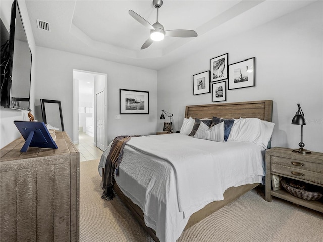 bedroom with ensuite bathroom, a tray ceiling, visible vents, and a ceiling fan