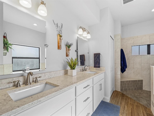 full bathroom with double vanity, visible vents, a sink, and wood finished floors