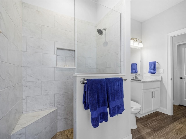 bathroom featuring toilet, a walk in shower, wood finished floors, and vanity