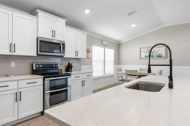 kitchen featuring appliances with stainless steel finishes, light wood-style floors, ornamental molding, wainscoting, and vaulted ceiling