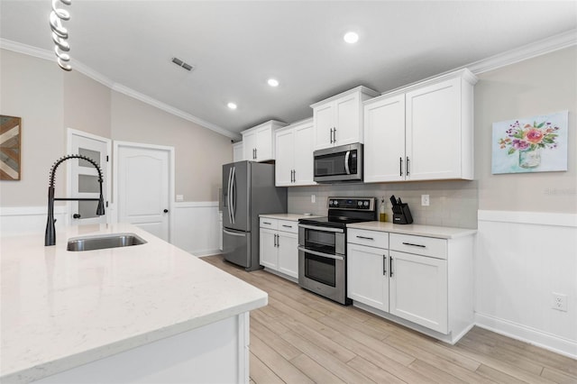 kitchen with lofted ceiling, stainless steel appliances, white cabinets, and crown molding