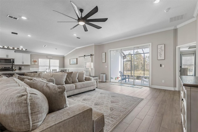 living room with lofted ceiling, light wood-style floors, a barn door, and ornamental molding