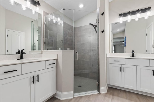 bathroom featuring two vanities, a sink, a shower stall, and wood finished floors