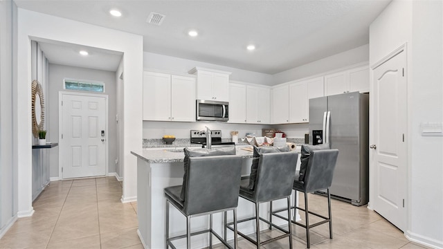 kitchen featuring a center island with sink, a breakfast bar area, visible vents, appliances with stainless steel finishes, and white cabinetry