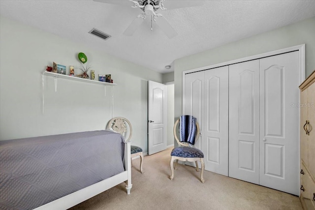 bedroom with ceiling fan, a textured ceiling, light carpet, visible vents, and a closet