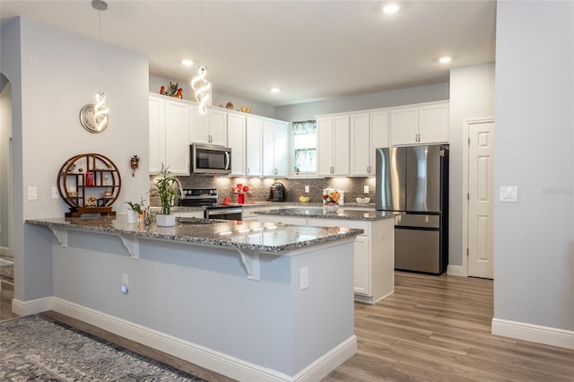 kitchen featuring hanging light fixtures, white cabinets, stainless steel appliances, and dark stone countertops