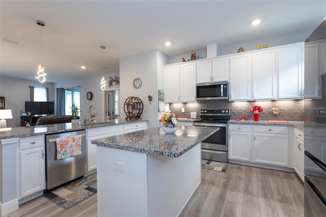 kitchen with appliances with stainless steel finishes, white cabinets, and decorative light fixtures