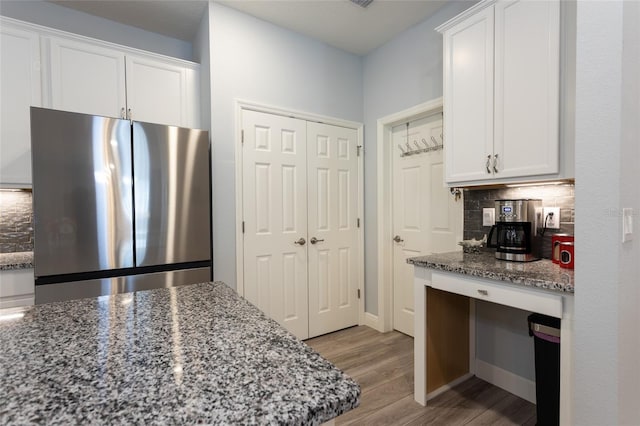 kitchen with stone countertops, backsplash, freestanding refrigerator, and white cabinets