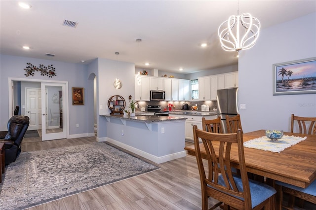 dining room featuring arched walkways, light wood-style flooring, recessed lighting, visible vents, and baseboards