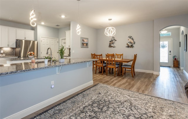 kitchen with stone counters, arched walkways, pendant lighting, freestanding refrigerator, and white cabinetry