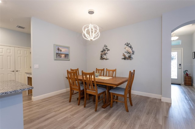 dining space with arched walkways, baseboards, a notable chandelier, and light wood finished floors