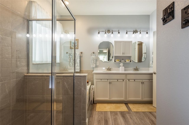 full bathroom with double vanity, a sink, a tile shower, and wood finished floors