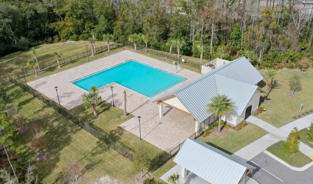 community pool with a patio area, fence, and a lawn