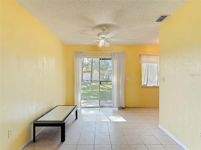 doorway featuring light tile patterned floors, a textured ceiling, visible vents, baseboards, and a ceiling fan