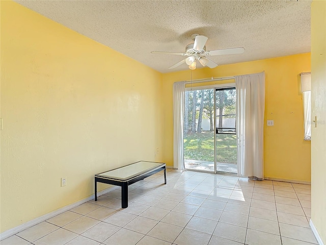 interior space with light tile patterned floors, a textured ceiling, a ceiling fan, and baseboards