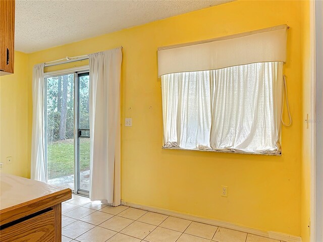 interior space with light tile patterned floors, a textured ceiling, a wealth of natural light, and baseboards