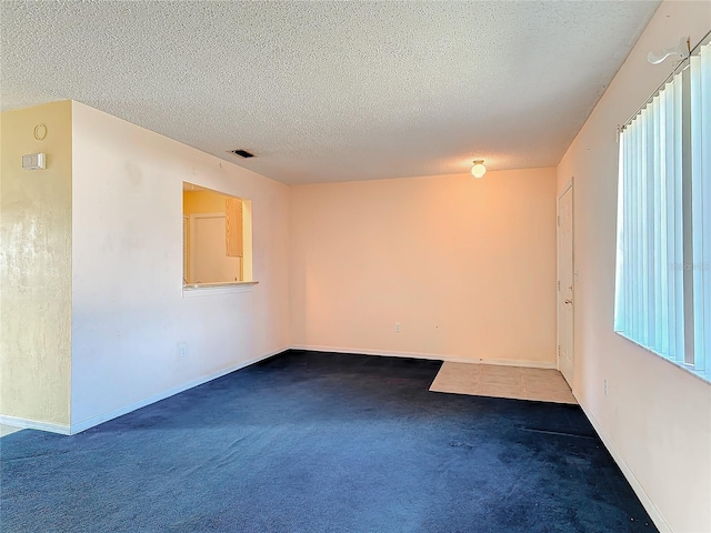 unfurnished room with dark colored carpet, a healthy amount of sunlight, and a textured ceiling