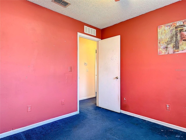 unfurnished room with a textured ceiling, dark colored carpet, visible vents, and baseboards