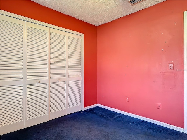 unfurnished bedroom with dark colored carpet, a closet, a textured ceiling, and baseboards