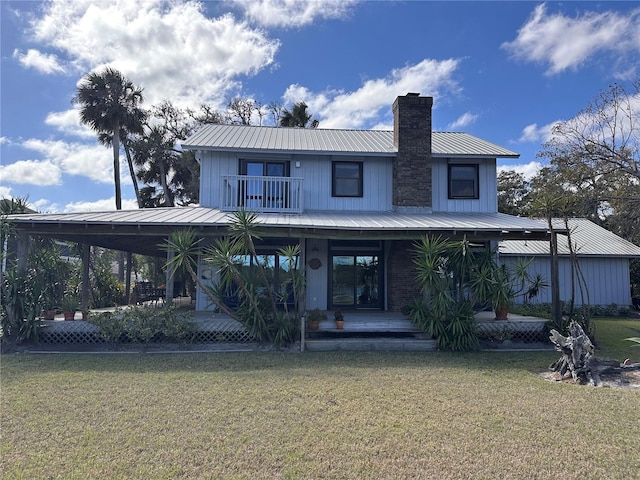 rear view of house featuring a balcony, a lawn, metal roof, and a chimney