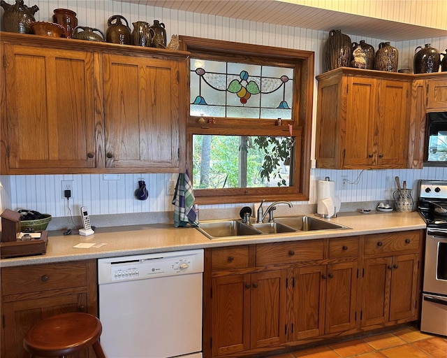 kitchen featuring white dishwasher, a sink, stainless steel range with electric cooktop, light countertops, and brown cabinetry