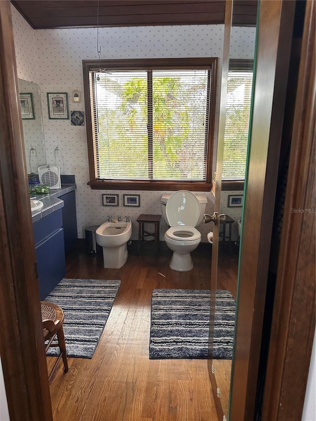 half bathroom featuring wallpapered walls, toilet, wood finished floors, a healthy amount of sunlight, and a bidet