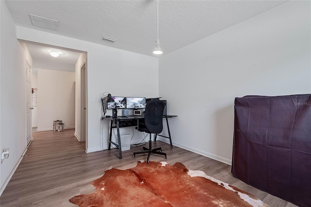 office featuring visible vents, a textured ceiling, baseboards, and wood finished floors