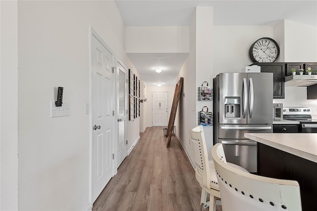 kitchen featuring light countertops, appliances with stainless steel finishes, ventilation hood, dark cabinetry, and light wood finished floors