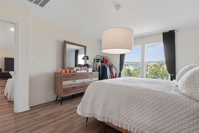 bedroom with visible vents, a textured ceiling, baseboards, and wood finished floors