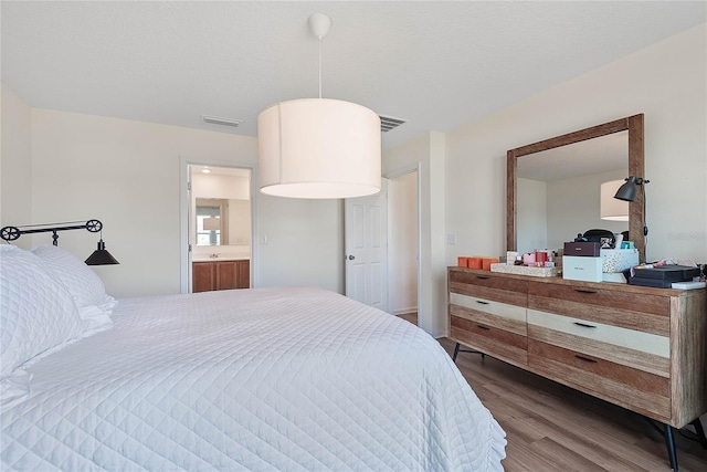 bedroom with a textured ceiling, visible vents, and wood finished floors