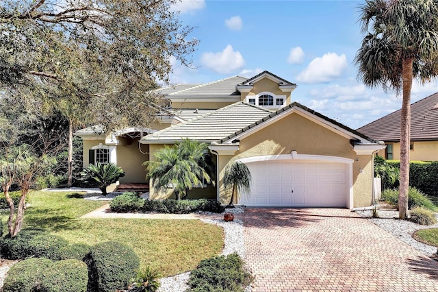 view of front of house with a front yard, decorative driveway, an attached garage, and stucco siding