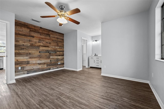 empty room featuring wood walls, dark wood finished floors, visible vents, and baseboards