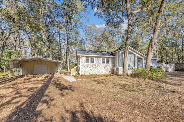 view of front of home with driveway, stone siding, a detached garage, and an outdoor structure