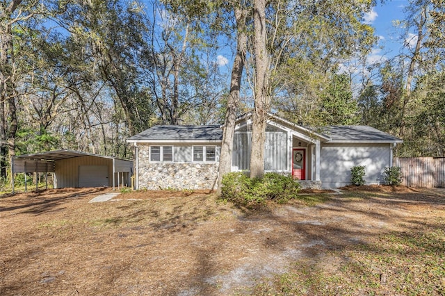 exterior space with an outbuilding, a detached garage, fence, stone siding, and driveway