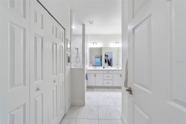 full bathroom with marble finish floor, a walk in shower, a textured ceiling, and vanity