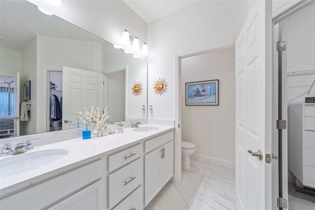 full bath with double vanity, a sink, toilet, and a walk in closet