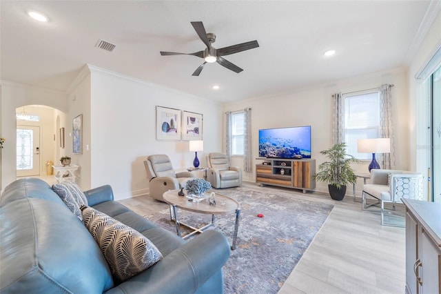 living room featuring a healthy amount of sunlight, light wood-style floors, arched walkways, and crown molding