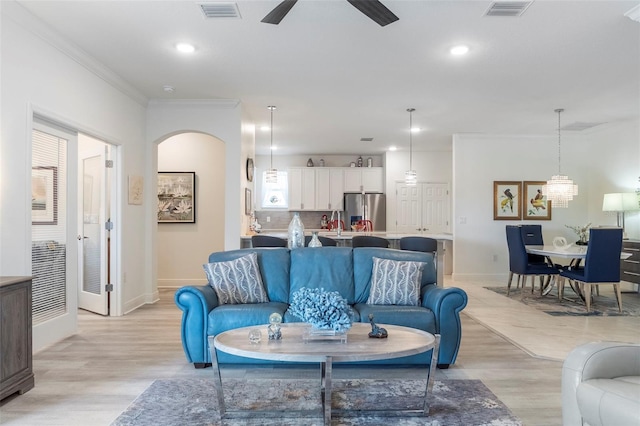 living room with light wood-style flooring, visible vents, arched walkways, and crown molding