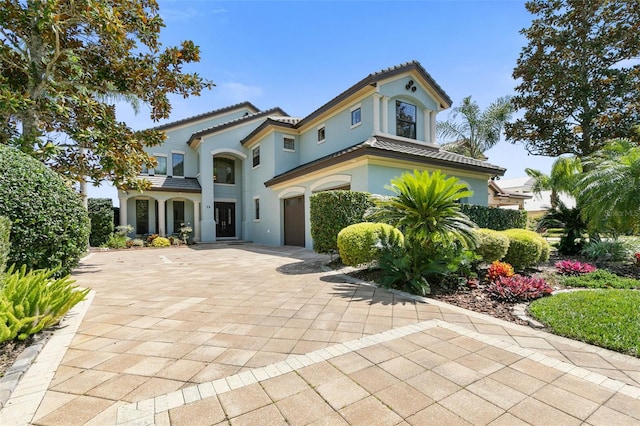 mediterranean / spanish-style house featuring a garage, decorative driveway, a tiled roof, and stucco siding