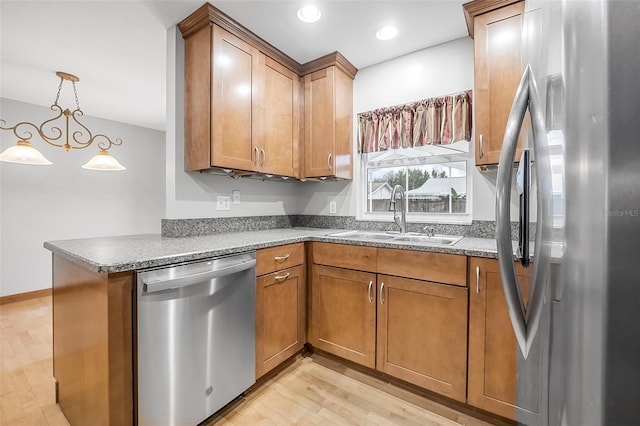 kitchen featuring a peninsula, a sink, appliances with stainless steel finishes, brown cabinetry, and decorative light fixtures