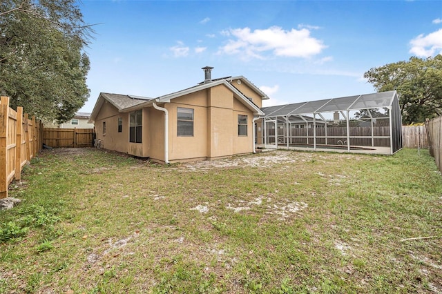 rear view of property featuring a fenced backyard, a lawn, a lanai, and stucco siding