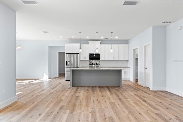 kitchen with a center island with sink, visible vents, stainless steel appliances, white cabinetry, and backsplash