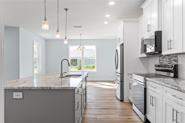 kitchen with a center island with sink, tasteful backsplash, appliances with stainless steel finishes, a sink, and light wood-type flooring