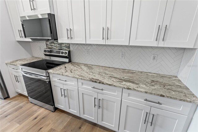 kitchen with white cabinets, light wood-type flooring, stainless steel appliances, and backsplash