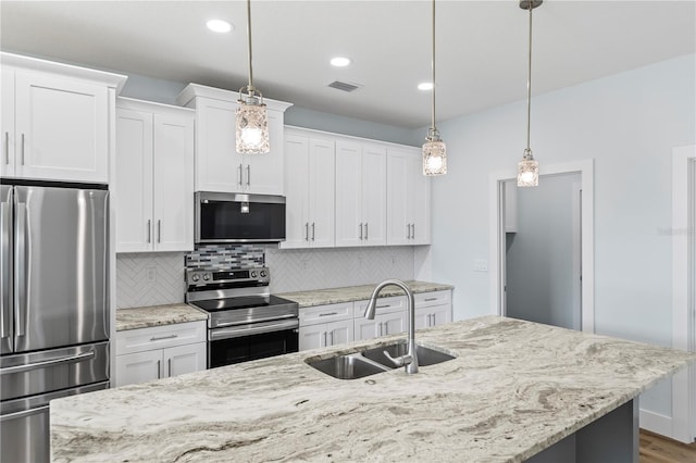 kitchen featuring pendant lighting, stainless steel appliances, decorative backsplash, white cabinetry, and a sink