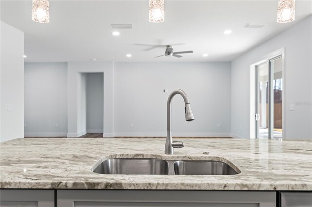 kitchen featuring open floor plan, light stone counters, a sink, and gray cabinetry