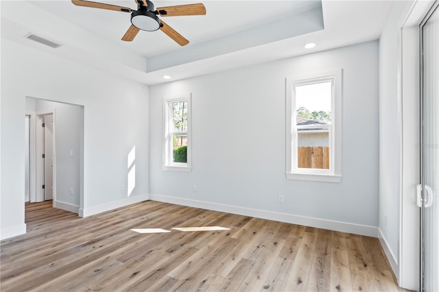 empty room with a healthy amount of sunlight, light wood finished floors, visible vents, and a raised ceiling